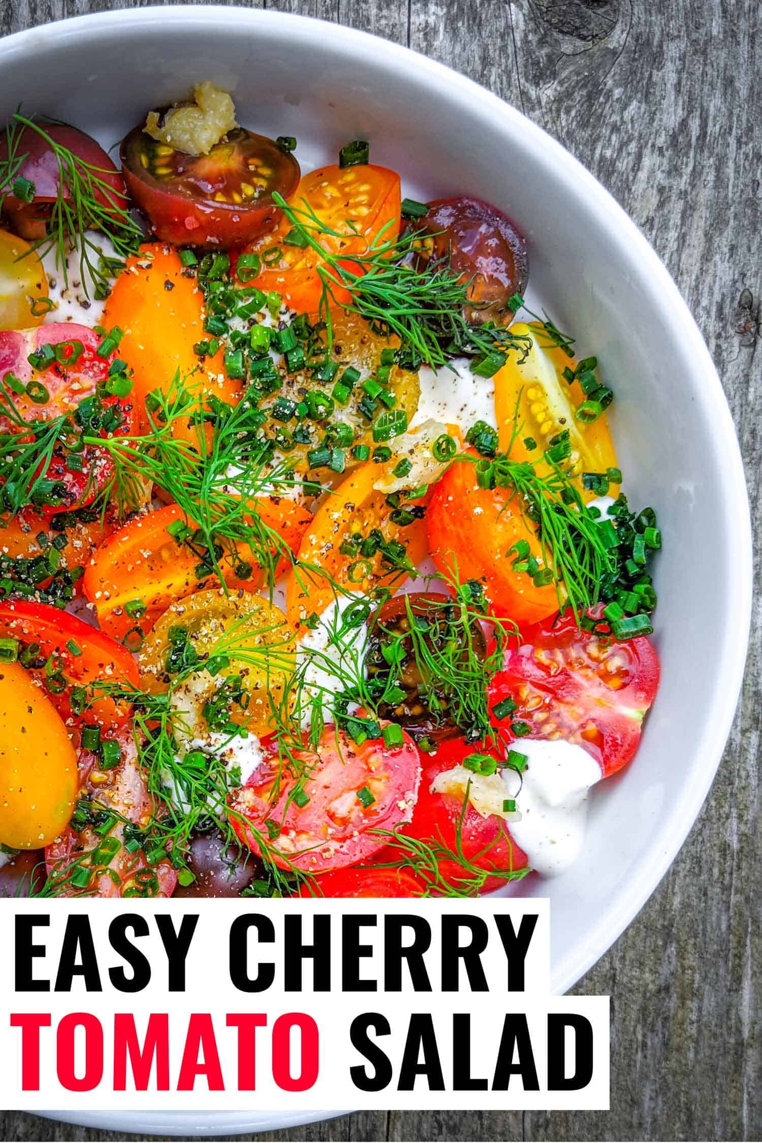 Fresh cherry tomato salad with herbs and creme fraiche in white bowl on grey wood background