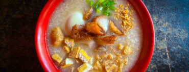 Traditional Filipino breakfast Lugaw in a red bowl on a wooden table