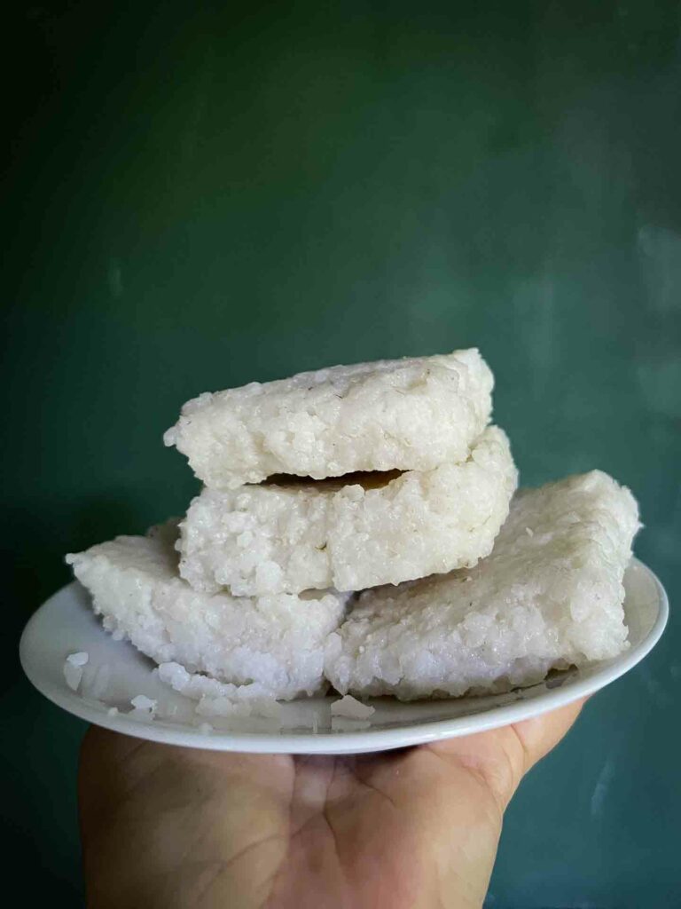 Delicious squares of Kiri Bath, a traditional Sri Lankan rice dish, neatly piled on a white plate, served alongside lunu miris sambol with chilis and maldives fish set against a rustic background in Ella, Sri Lanka.