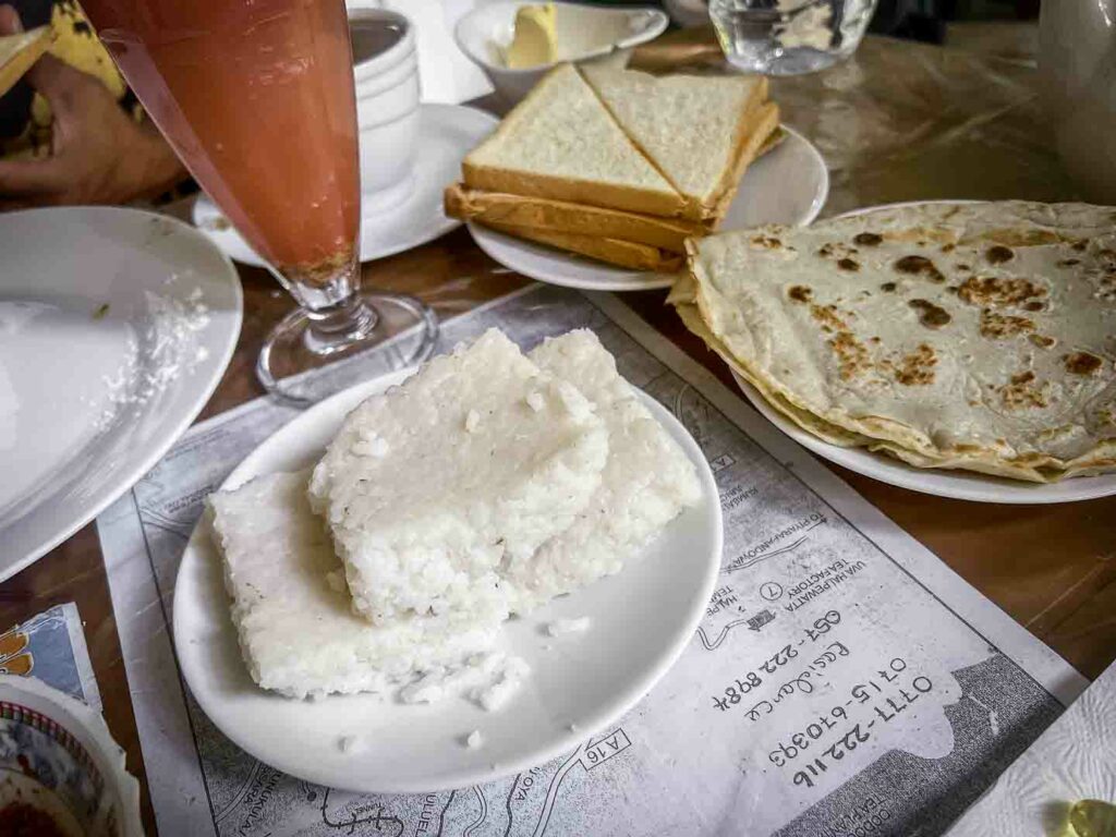 Delicious squares of Kiri Bath, a traditional Sri Lankan rice dish, neatly piled on a white plate, served alongside lunu miris sambol with chilis and maldives fish set against a rustic background in Ella, Sri Lanka.