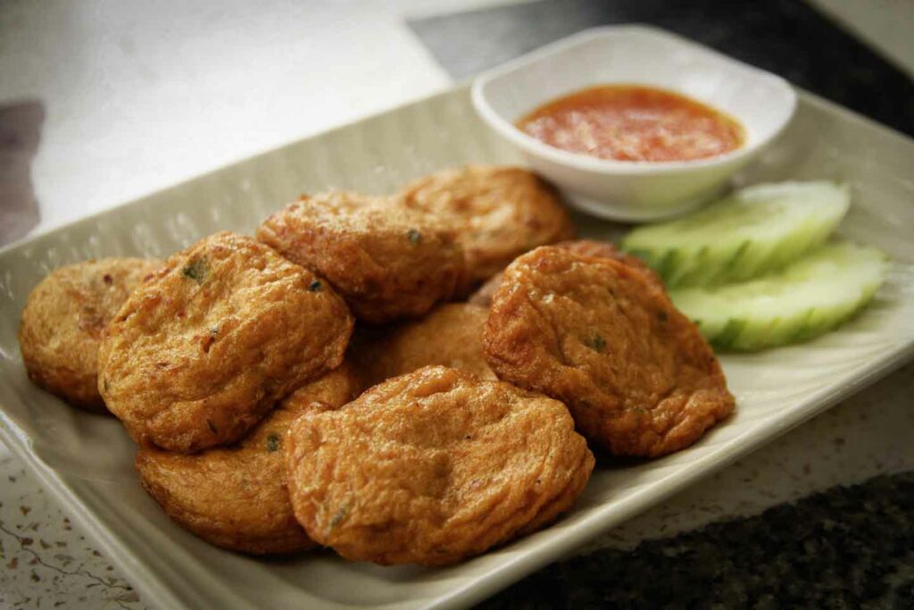 Thai fish cakes on white plate with sweet chili sauce and cucumber