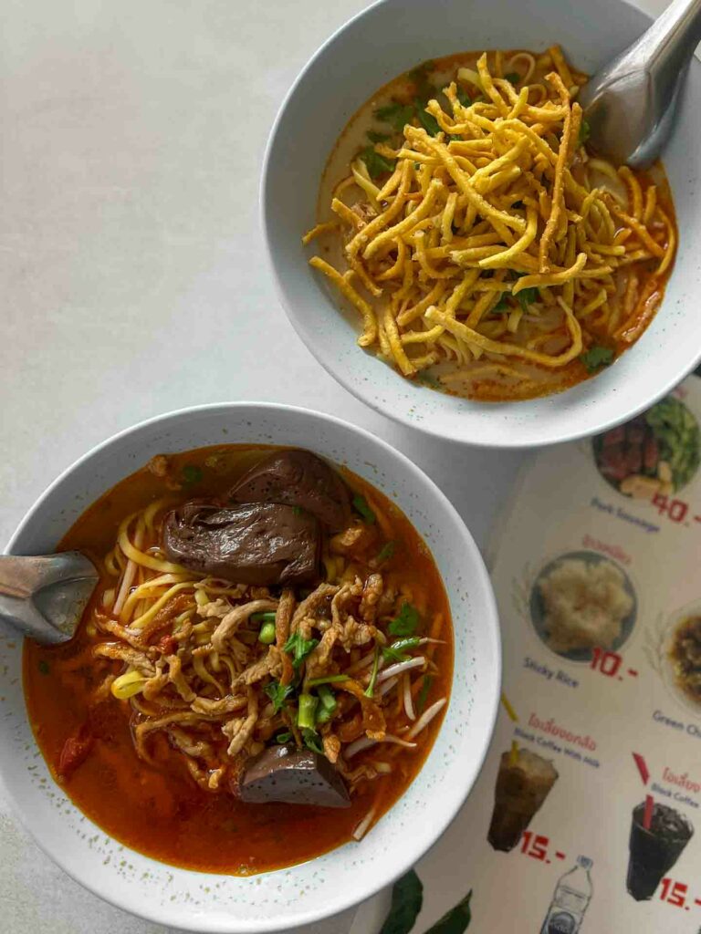 Two types of khao soi on table, one bright red from Chiang Rai and the other from Chiang Mai and typical orange color