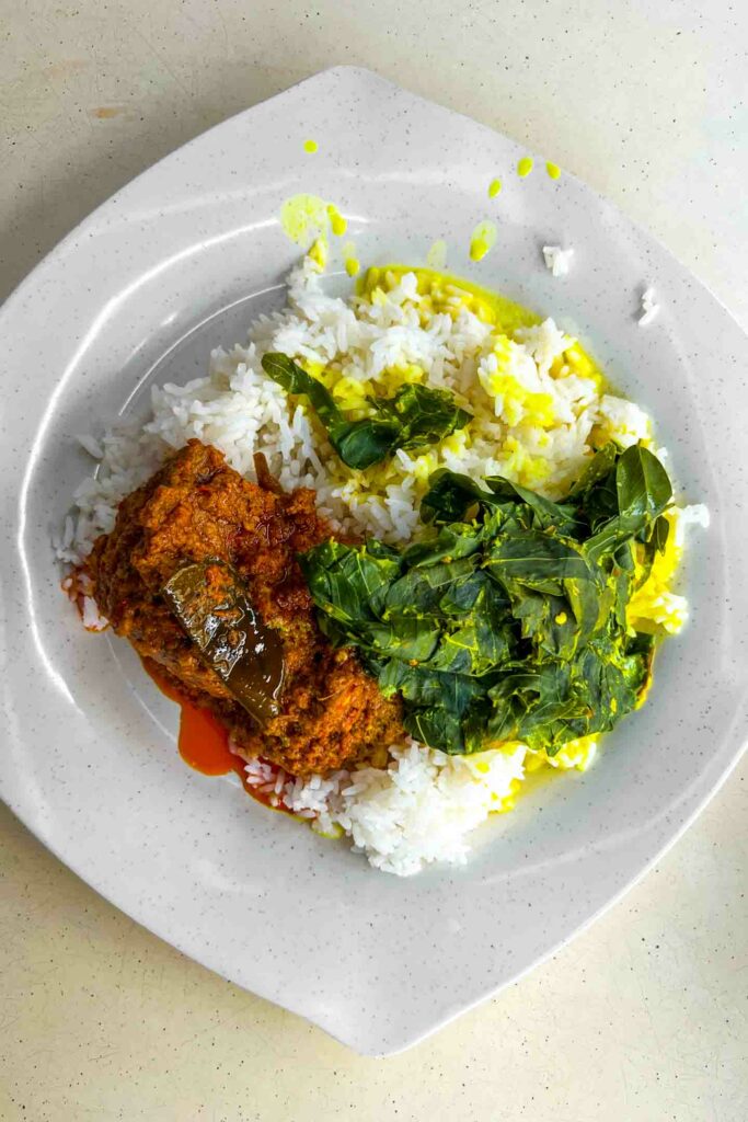 Nasi lemak, traditional breakfast in Singapore with coconut rice, greens and rendang on a white plate and white table in restaurant